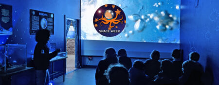Children in a classroom at an aquarium. The room is blue and gives the impression of being under the sea.